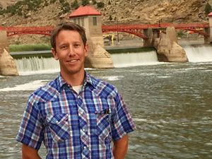 A man in a plaid shirt standing in front of dam full of water.