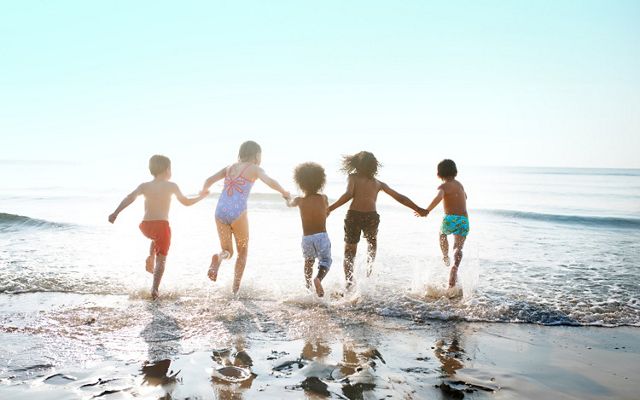 Five children hold hands and run into the ocean with their backs turned to the camera.