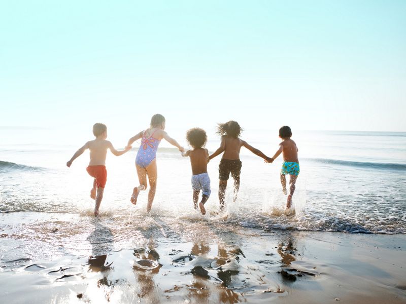 Five children hold hands and run into the ocean with their backs turned to the camera.
