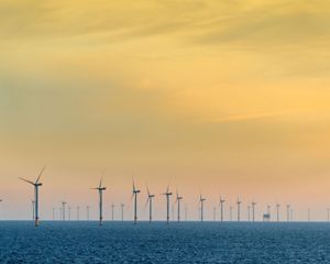 An offshore windfarm against a yellow sky