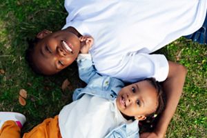 Two children lay in the grass laughing at the camera. 