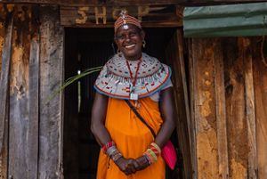 A woman stands in front of a wood structure that says 'shop'.