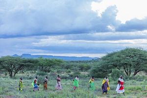 A wide shot of a group of women walking in a line in a lush Kenya landscape.