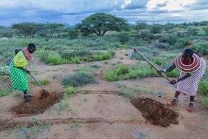 Two women use spades to dig a hole in the Kenyan soil.