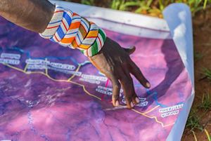 A hand with beaded bracelets on the wrist points at a map.