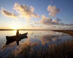 A person in a canoe pauses on calm waters as the sun sets.