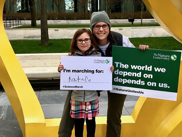 A woman at right with a sign in her hand saying "The world we depend on depends on us." next to a younger individual holding a sign saying "I'm marching for nature."