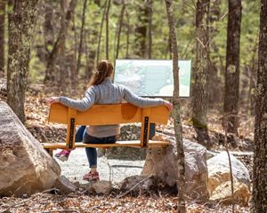 A woman sitting on a bench in the woods.