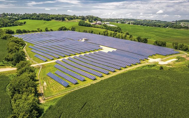 Solar energy farm amid green farmfields and blue sky.