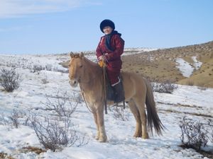 A woman sits atop her horse on snow-covered grasslands in Mongolia