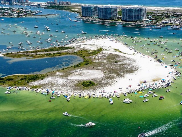 aerial image of a small sandy island surrounded by dozens of boats.