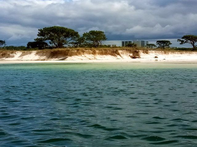View from the water of a coastline with sandy bluffs eroding down to the beach.