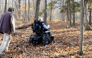 A person rides an all-terrain wheel trail through a leafy trail in a wooded landscape.