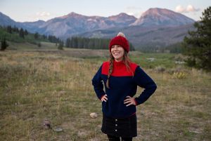a woman in a hat and jacket with her hands on her hips.