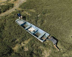 Two men push a boat across a dried-up riverbed of grasses.