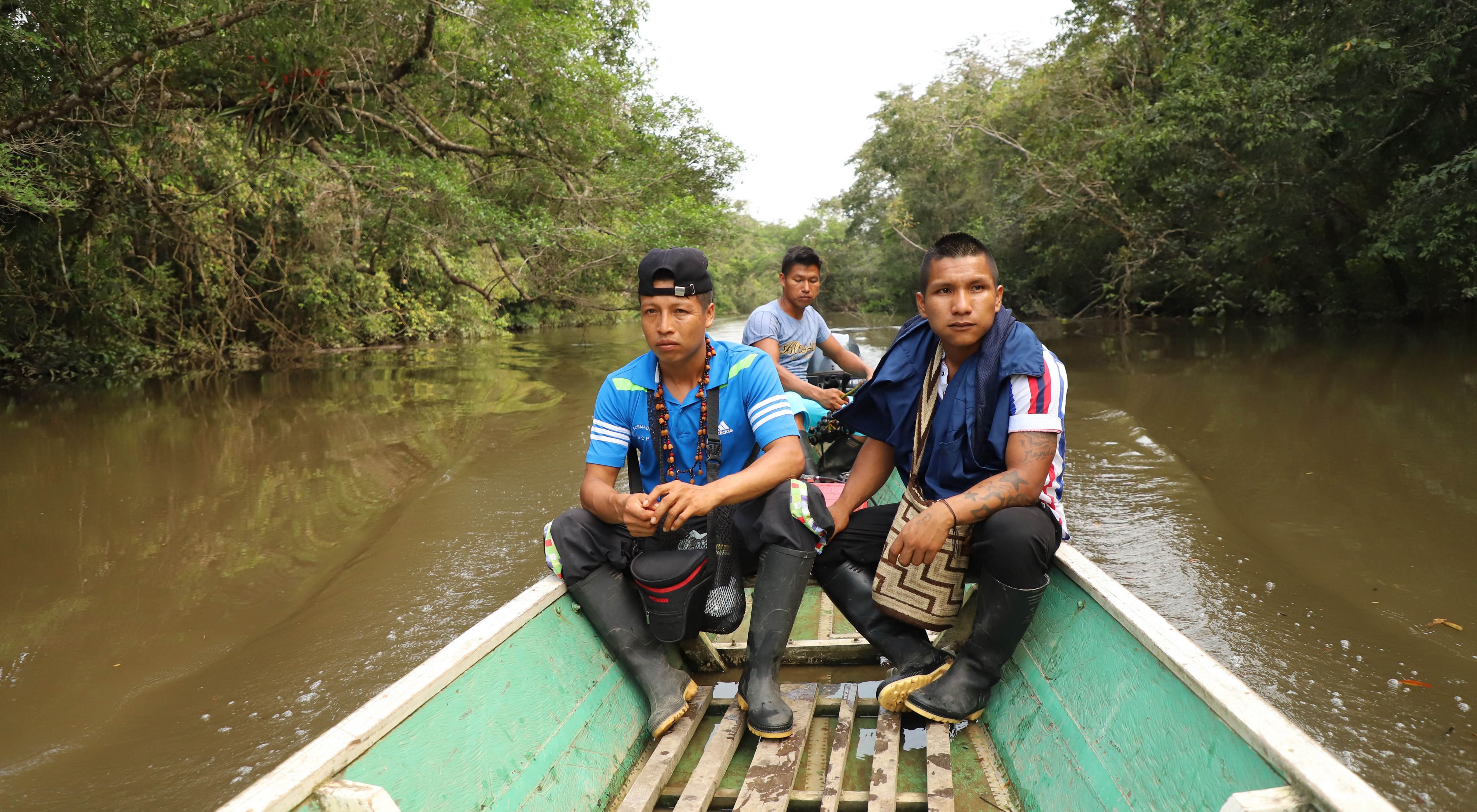 Three men from an Indigenous community in the Amazon rainforest are in the stern of a boat, travelling upriver.