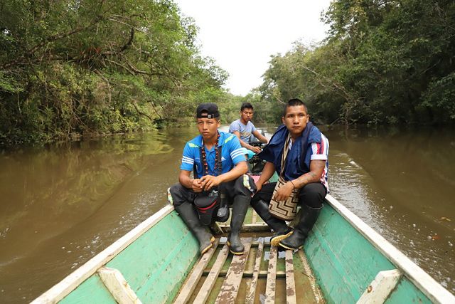 Foto de tres jóvenes en una pequeña embarcación de pesca recorriendo un afluente del río Amazonas.
