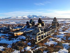 People sit on snowmobiles in a melting snow landscape