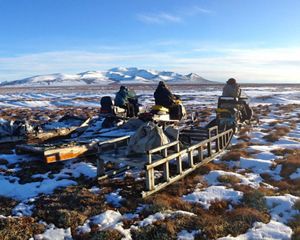 People sit on snowmobiles in a melting snow landscape