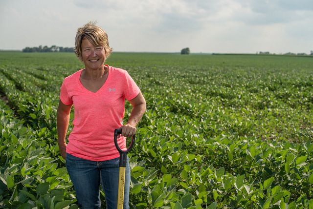 A woman in a pink shirt standing in a planted field of soybean crops.