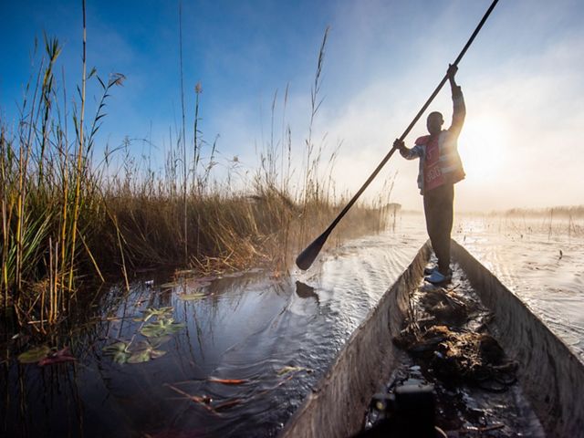 A man stands on a gondola holding a long paddle.