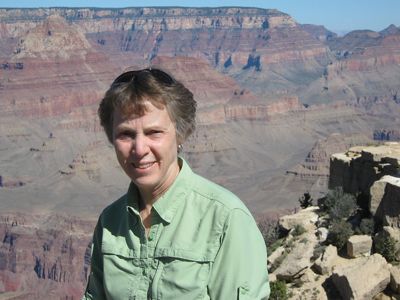 A close-up features a woman wearing a green shirt smiling in front of the Grand Canyon National Park.