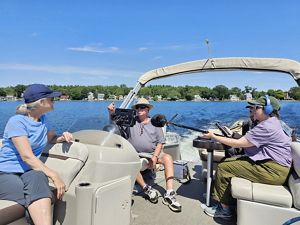 Four people sit on a boat in the middle of one of the APC ponds, two podcast producers with mics and gear, Tom Barron, who is piloting the boat, and Marea Gabriel of TNC.