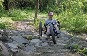 A person wearing a helmet rides a three wheeled bike over a rocky trail.
