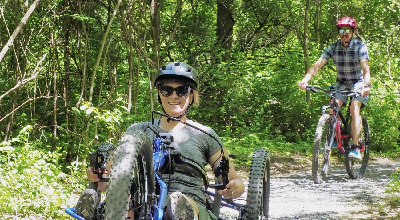 A adaptive bike user and mountain biker on a trail.