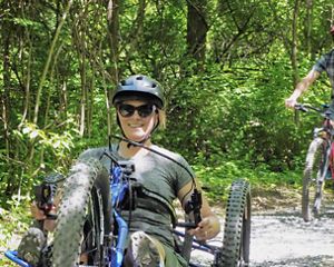 An adaptive biker and mountain biker on a trail.