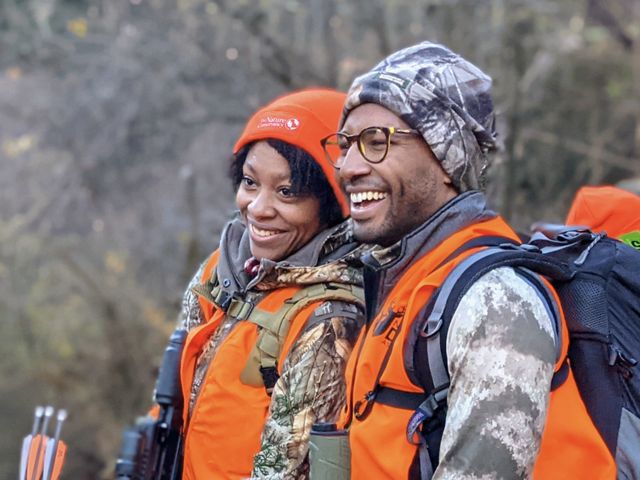 Two people in hunting gear looking off to the side and laughing.