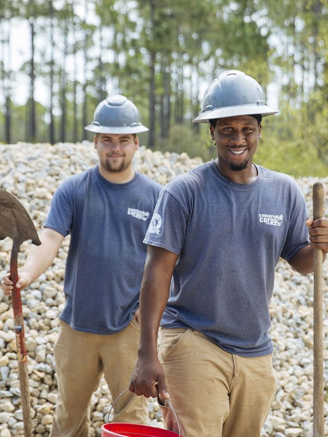 Two young men in hard hats holding shovels.