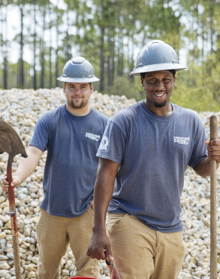 Two young men in hard hats holding shovels.