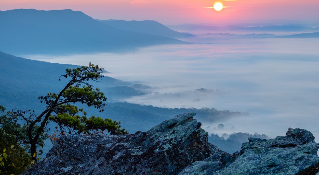 The sun rises over a foggy mountain valley.