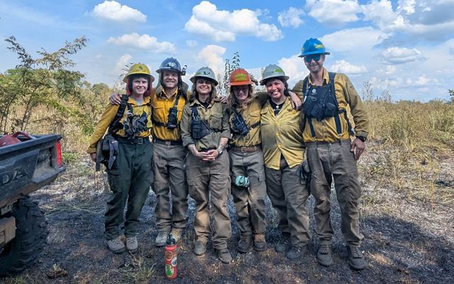 Group of fire crew pose in front of a recently burned field.