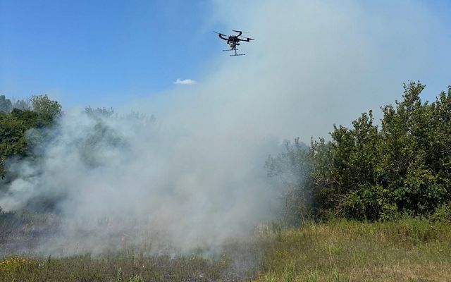Drone flies in sky over smoke from fire.