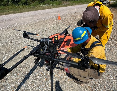 Two fire crew members working on a large drone.