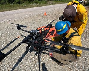 Two fire crew members working on a large drone.