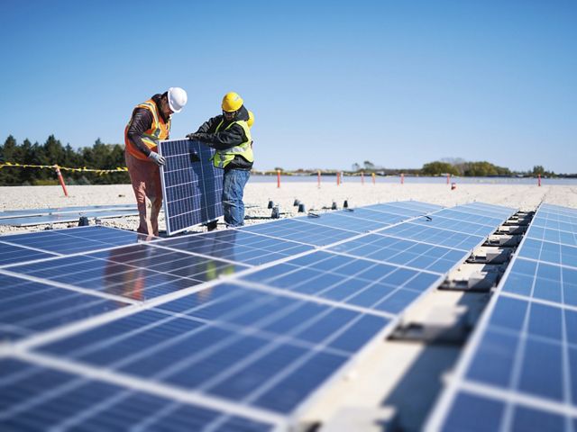 Two people installing solar panels while wearing jackets and hard hats. 