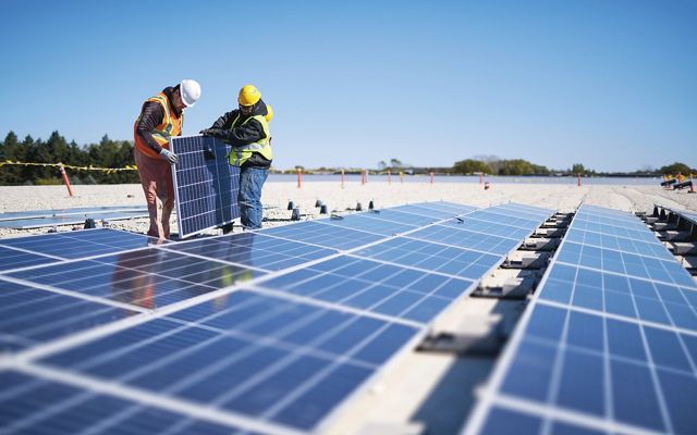 dos trabajadores llevan un panel solar que se instalará en una fila de paneles en tierra sucia