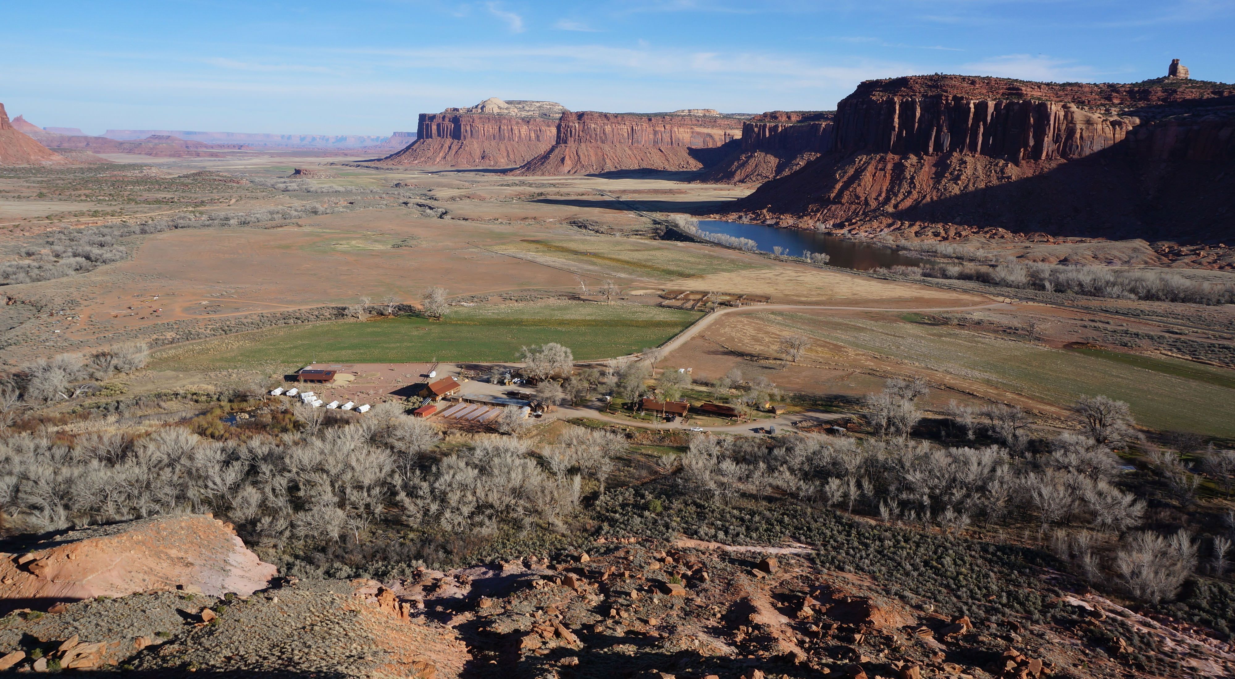 Aerial view of Canyonlands Research Center in a large valley surrounded by red cliffs under blue sky.
