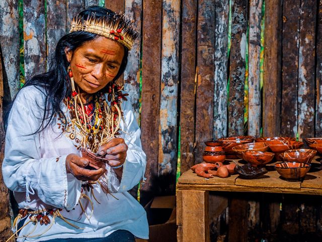 A woman in her traditional attire handles pottery crafts with a smile.