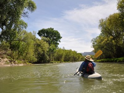 A person in a kayak sits on a river with vegetation on each side of it. 