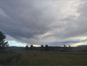 Blue sky peeks from behind a massive storm cloud that fills the sky overing a darkening landscape.