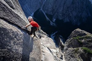 A rock climber clings to the edge of a sheer granite rock face.
