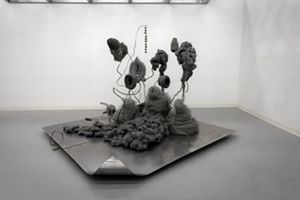 Abstract gray fiber sculpture features wire forms displayed on a metal platform in a gallery.