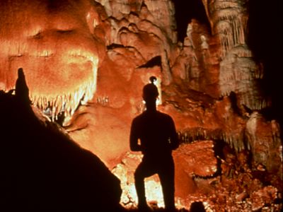 The silhouette of a person stands in a lit-up,  orange cave. 
