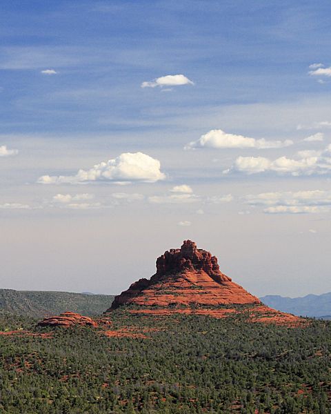 A wide, landscape view of a red rock formation with a blue sky above. 