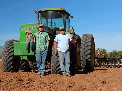 Three adults and a child stand in front of a green tractor on a sunny day. 