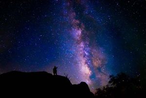 View of a person's silhouette in front of a purple night sky with stars, where the Milky Way Galaxy is visible.